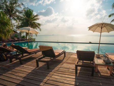 A serene beachfront pool with lounge chairs and umbrellas on a wooden deck.